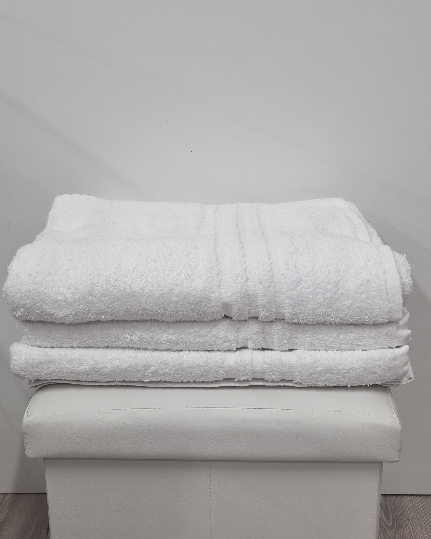 Asciugamani bianchi soffici piegati su pouf, articoli bagno di qualità per casa