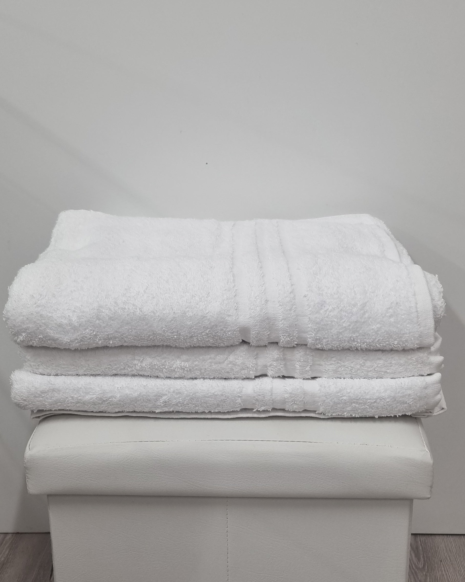 Asciugamani bianchi soffici piegati su pouf, articoli bagno di qualità per casa